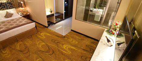 Habitación de hotel con cama, baño con ducha de vidrio, una kitchenette pequeña y televisión.
