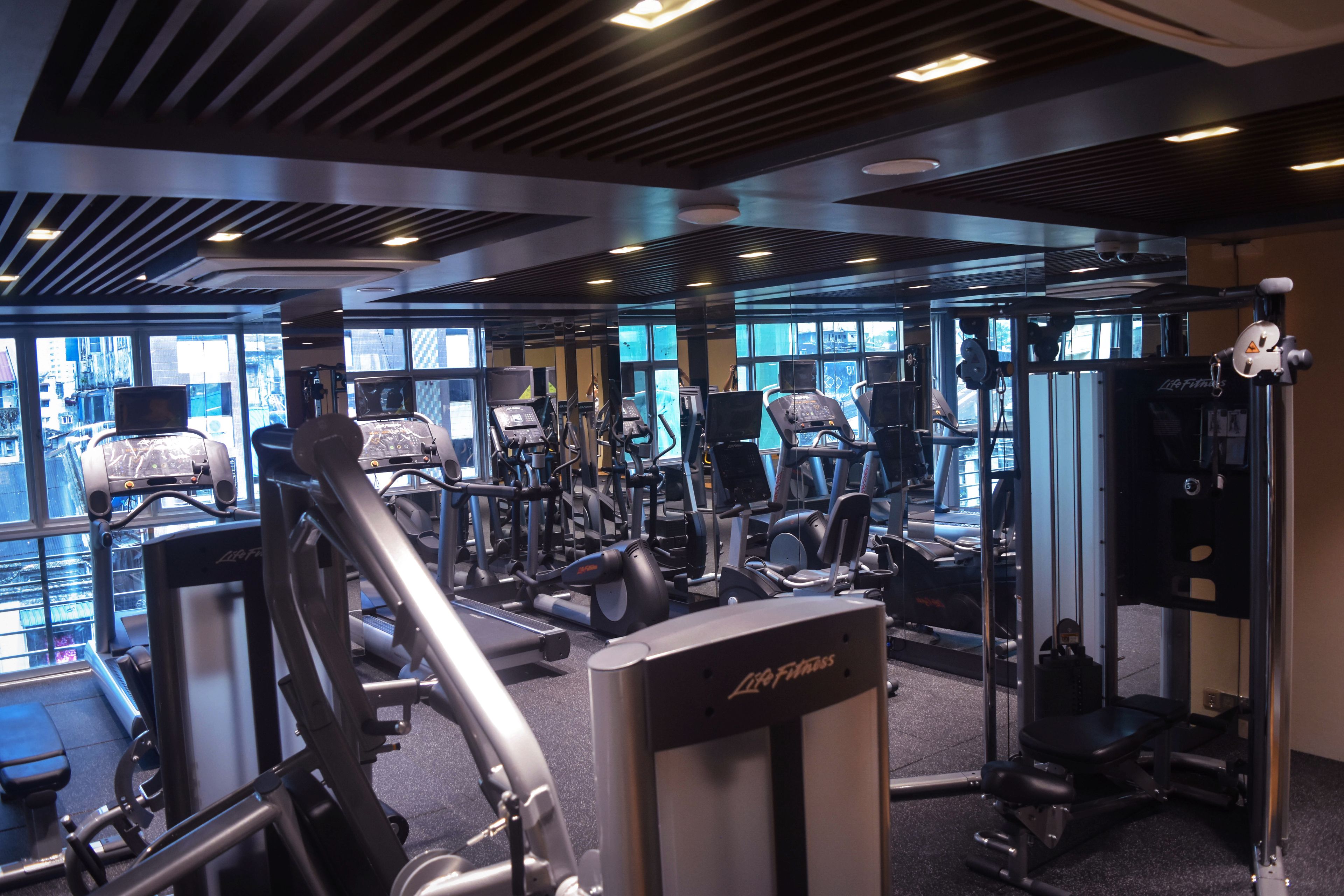 Une salle de sport équipée de divers appareils d’exercice, dotée de grandes fenêtres et d’un design moderne au niveau du plafond.