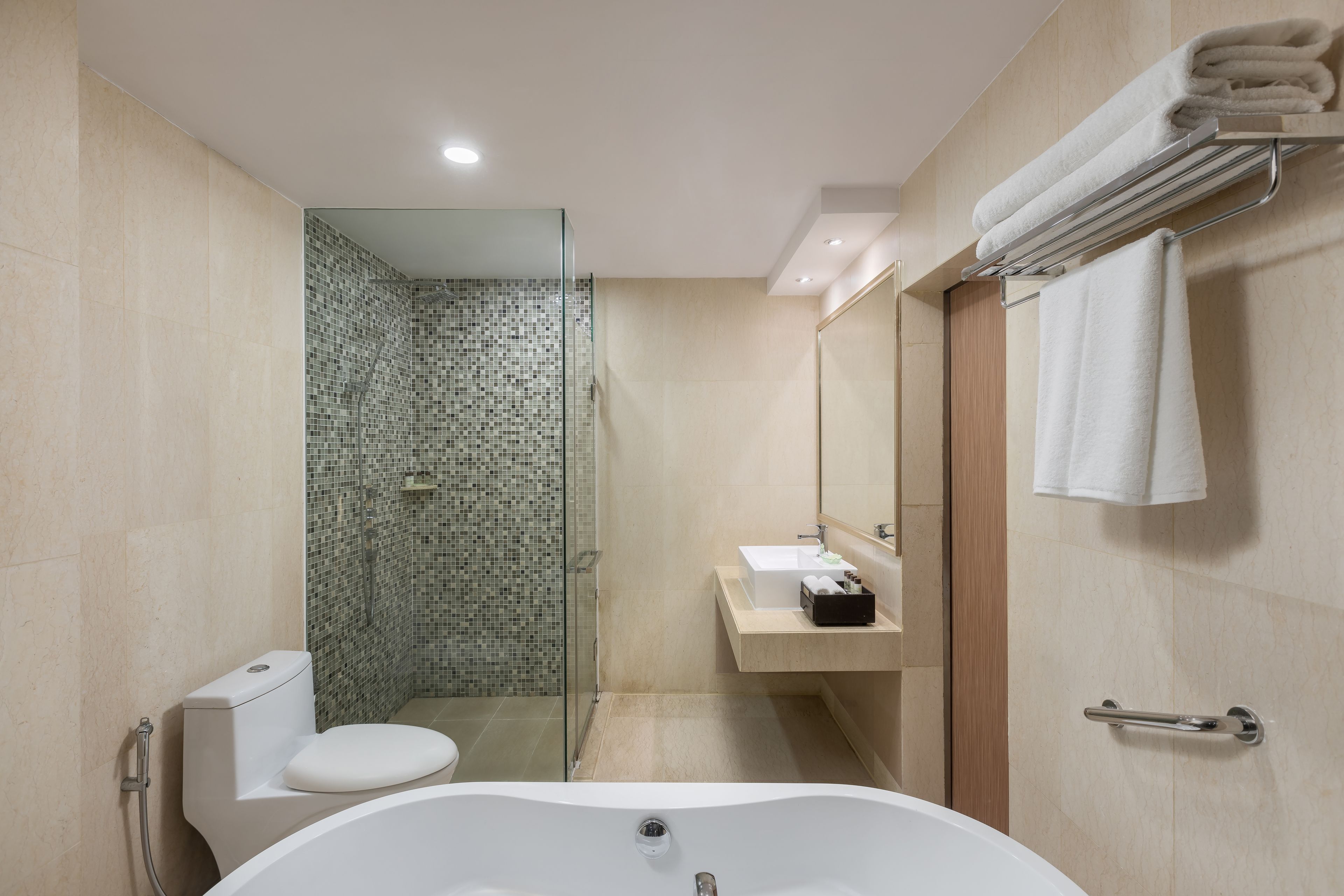 Un baño moderno con ducha de vidrio, inodoro blanco, bañera independiente y tocador con espejo y perchero.