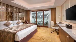 Quarto de hotel moderno com cama grande, escrivaninha, televisão e varanda com vista para edifícios.