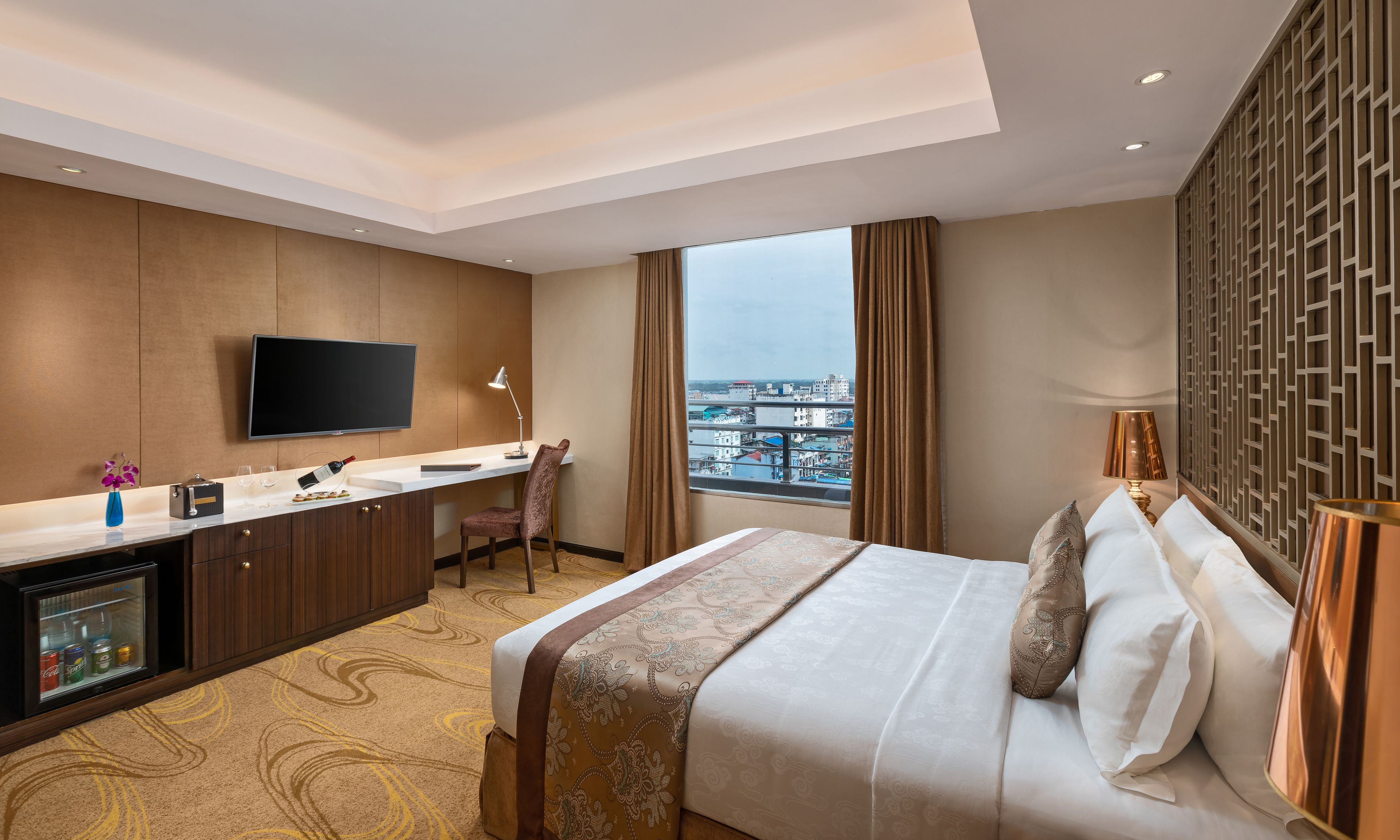 Habitación de hotel con cama, escritorio, televisión y vista a la ciudad.