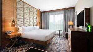 A hotel room with a bed, bedside table, lamp, TV, and a small table with a chair. - DoubleTree by Hilton Krakow Hotel & Convention Center (Kraków)