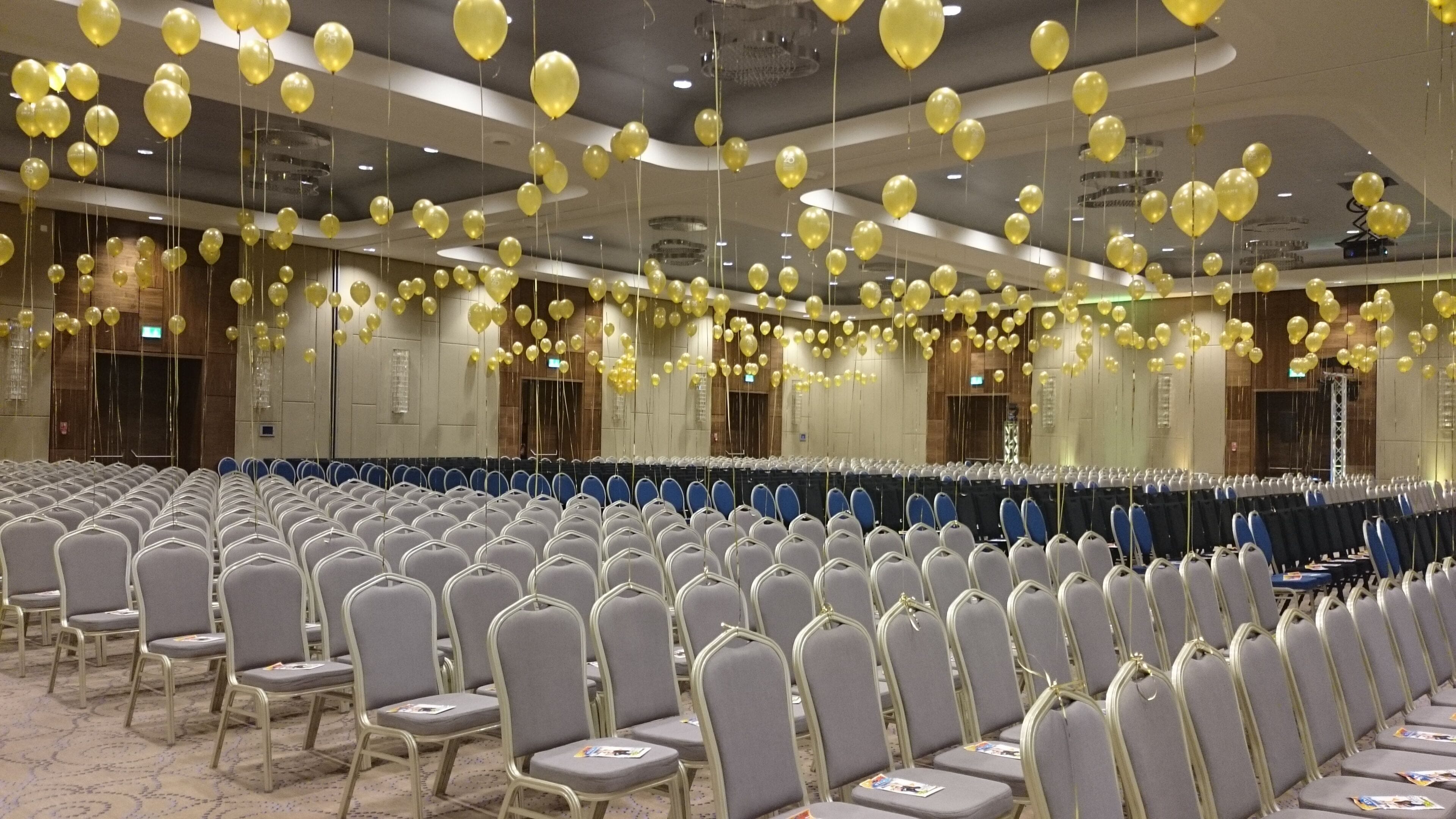A conference room with rows of chairs, a long table, and yellow balloons hanging from the ceiling.