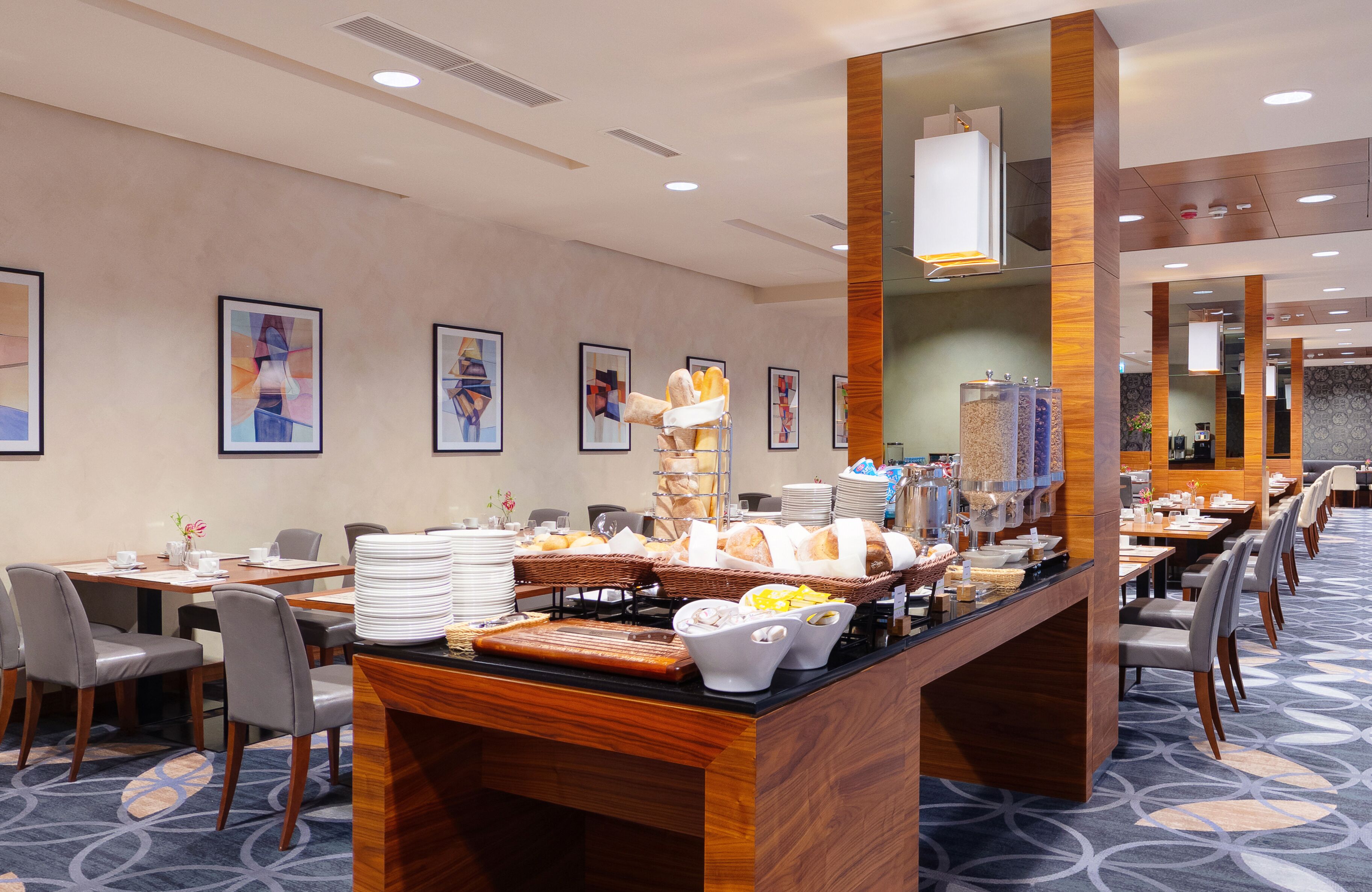 Un espace pour le petit-déjeuner à l’hôtel, aménagé avec un buffet, des tables, des chaises et des œuvres d’art encadrées accrochées aux murs.