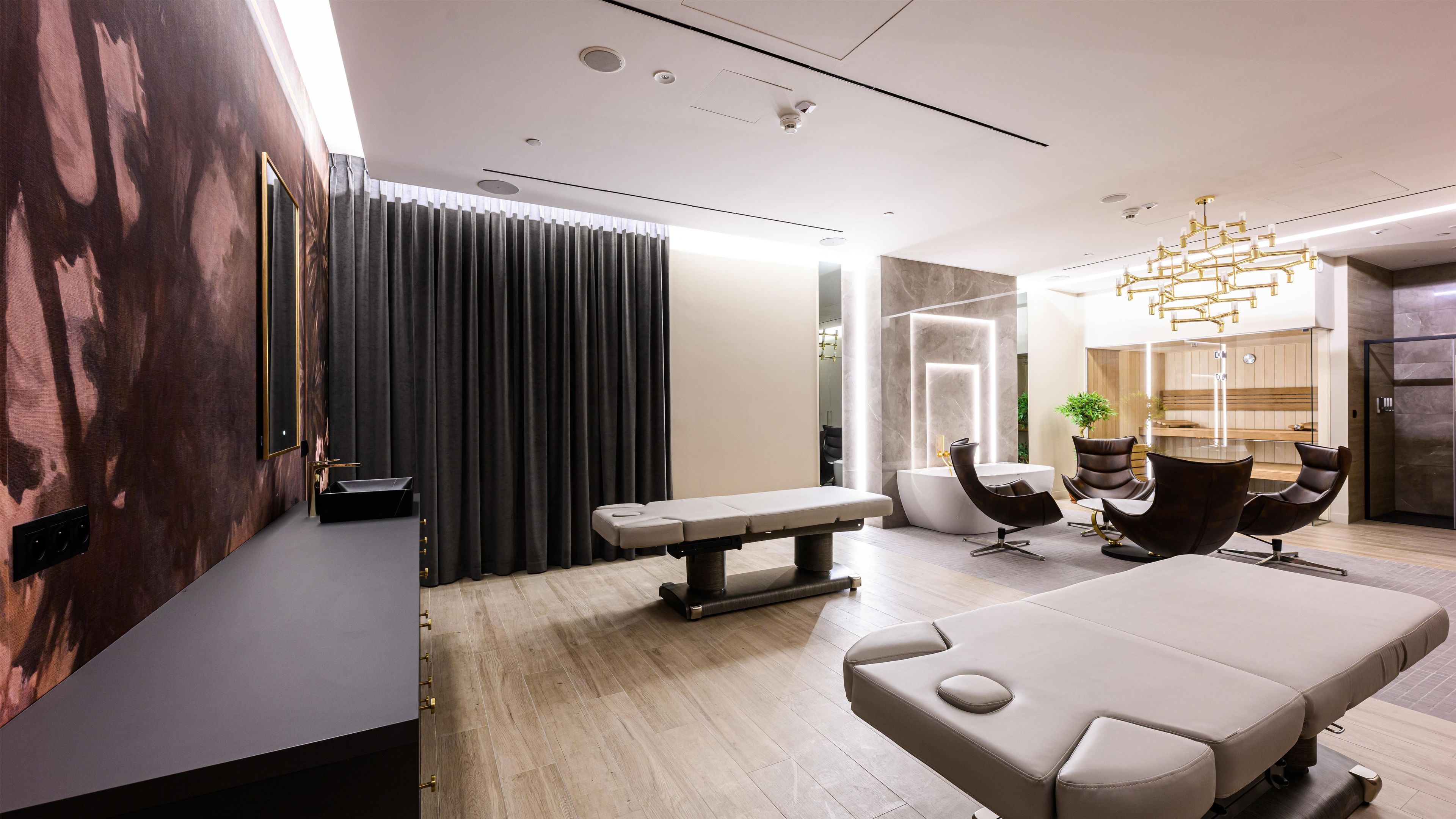 A modern spa room with a massage table, a bench, and a seating area with chairs.