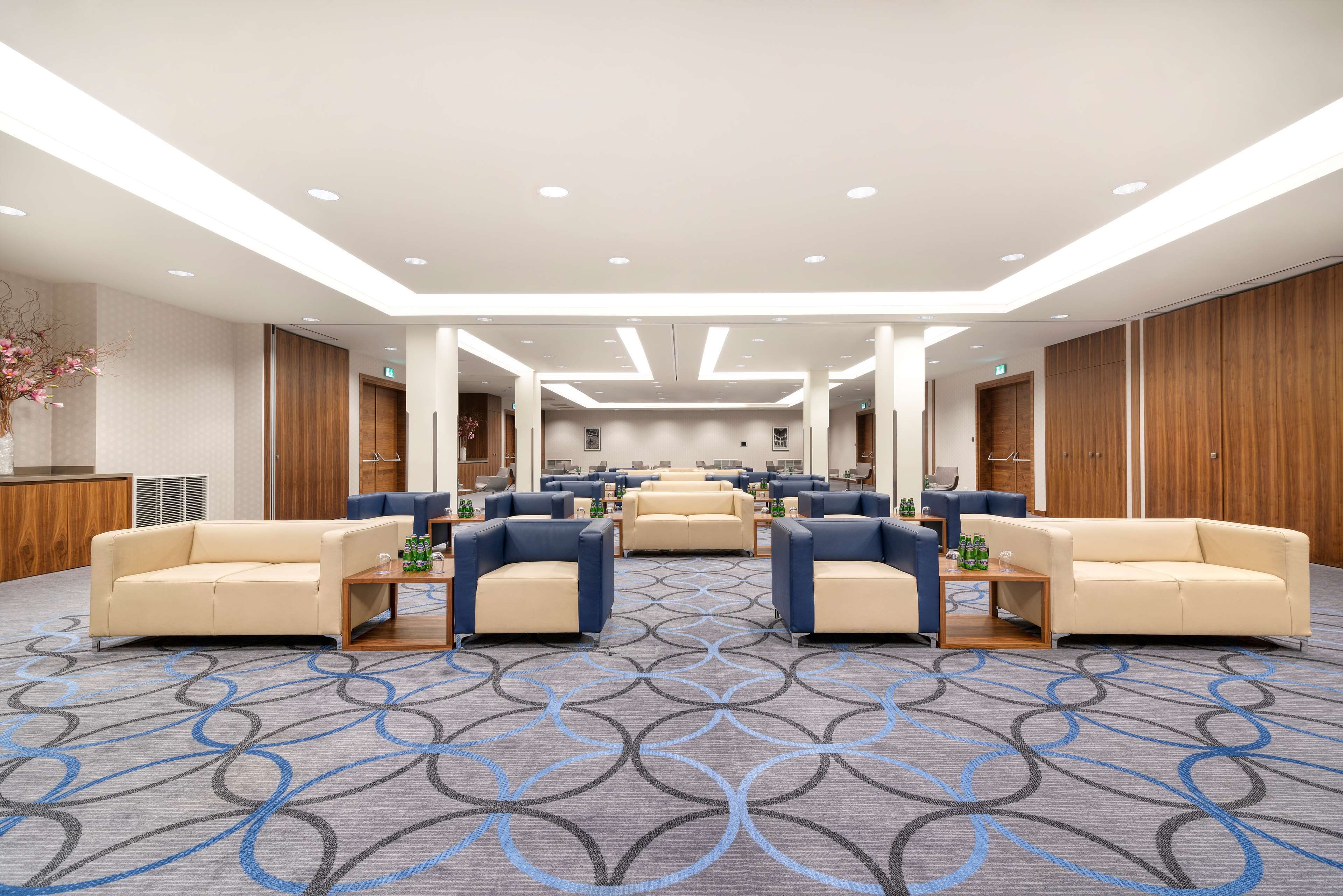 A spacious hotel lobby with multiple seating areas, a patterned carpet, and modern lighting.