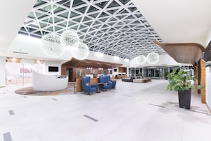 Un hall d’entrée spacieux avec un plafond haut, des sièges modernes et un comptoir d’accueil.