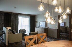 A hotel room with a sofa, a dining table, chairs, a TV, and multiple hanging light fixtures. - DoubleTree by Hilton Krakow Hotel & Convention Center (Kraków)