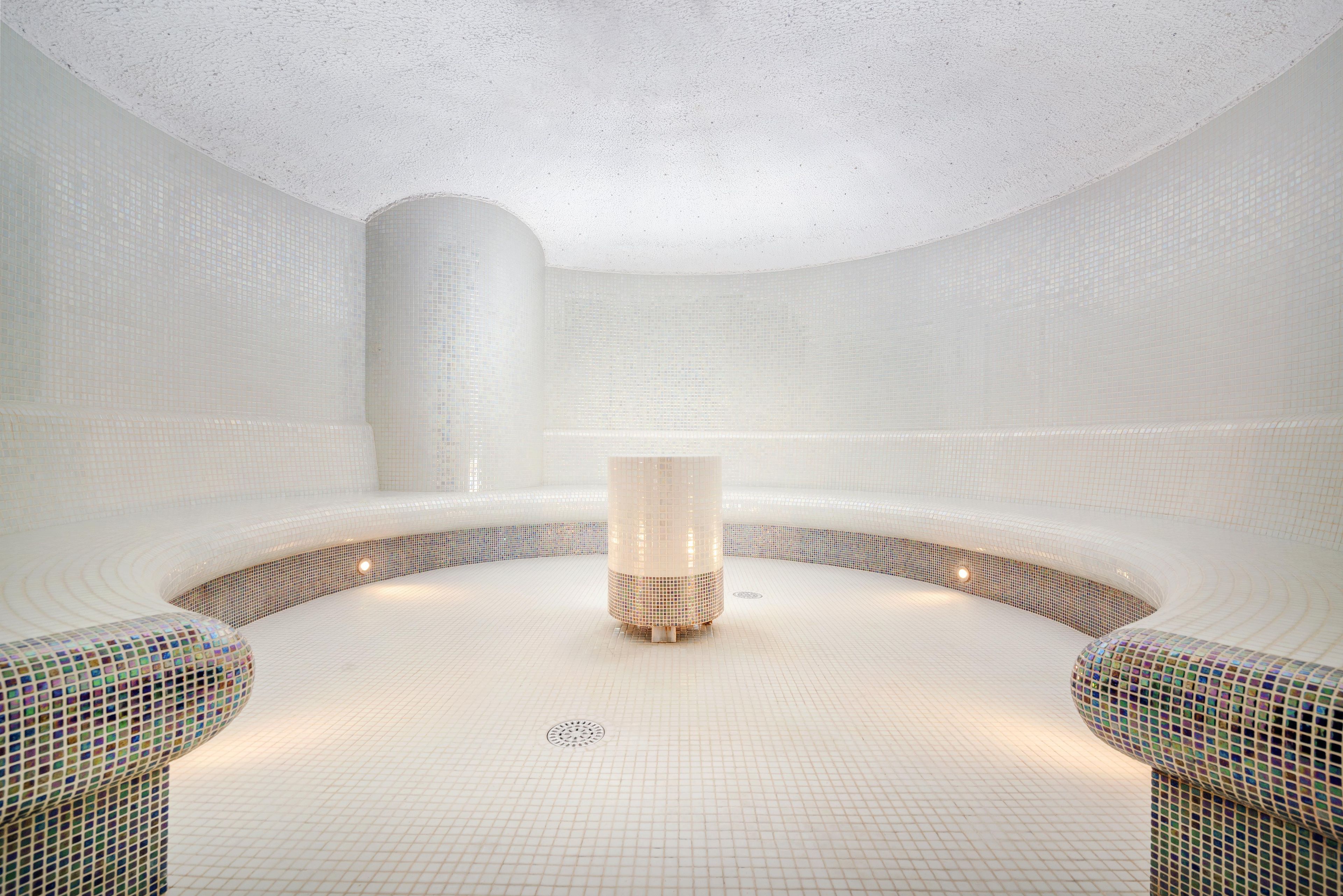 A modern spa room with a central column, tiled walls, and a circular seating area.