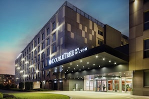 Un hôtel à l’architecture moderne, avec une enseigne « DOUBLETREE by Hilton » bien visible et une entrée bien éclairée.