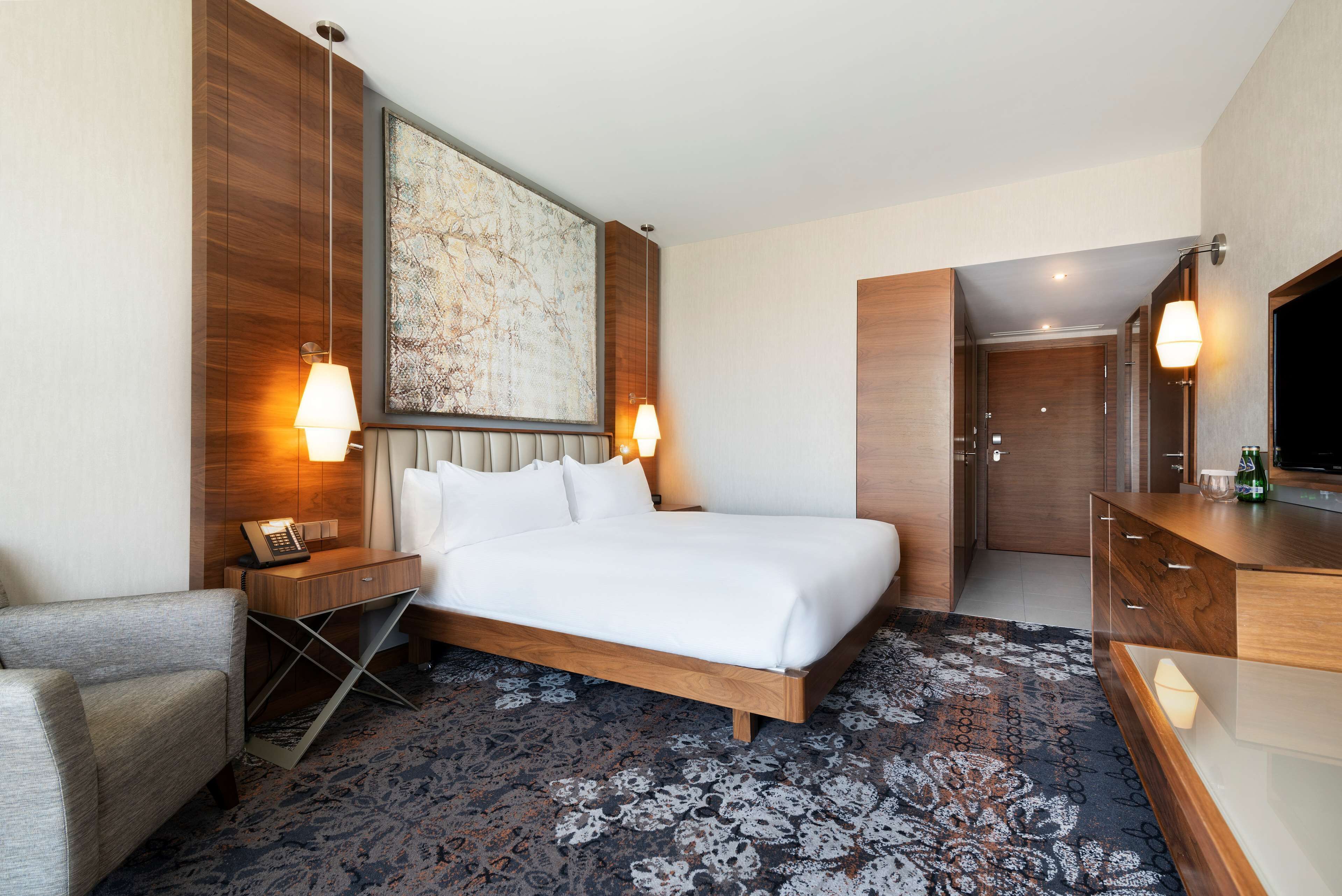 Una habitación de hotel con una cama grande, un escritorio con lámpara, una silla, un armario y un televisor.