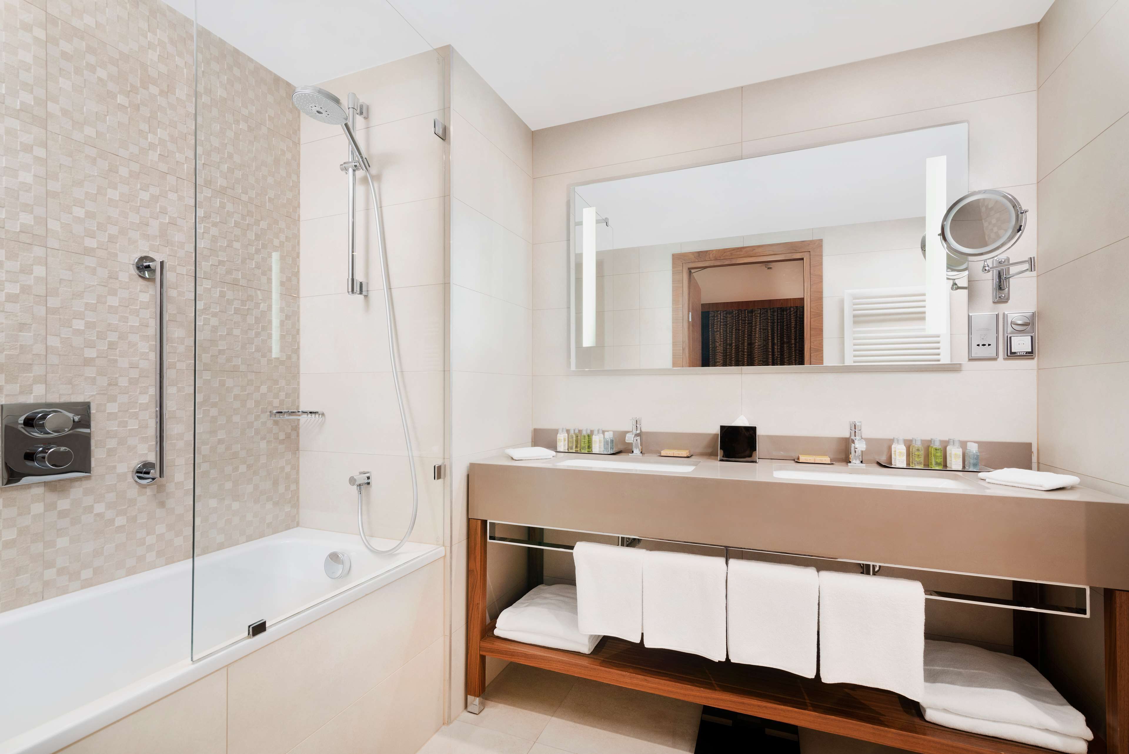 A modern bathroom with a glass-enclosed shower, a wooden vanity with a mirror, and a built-in shelf for towels.
