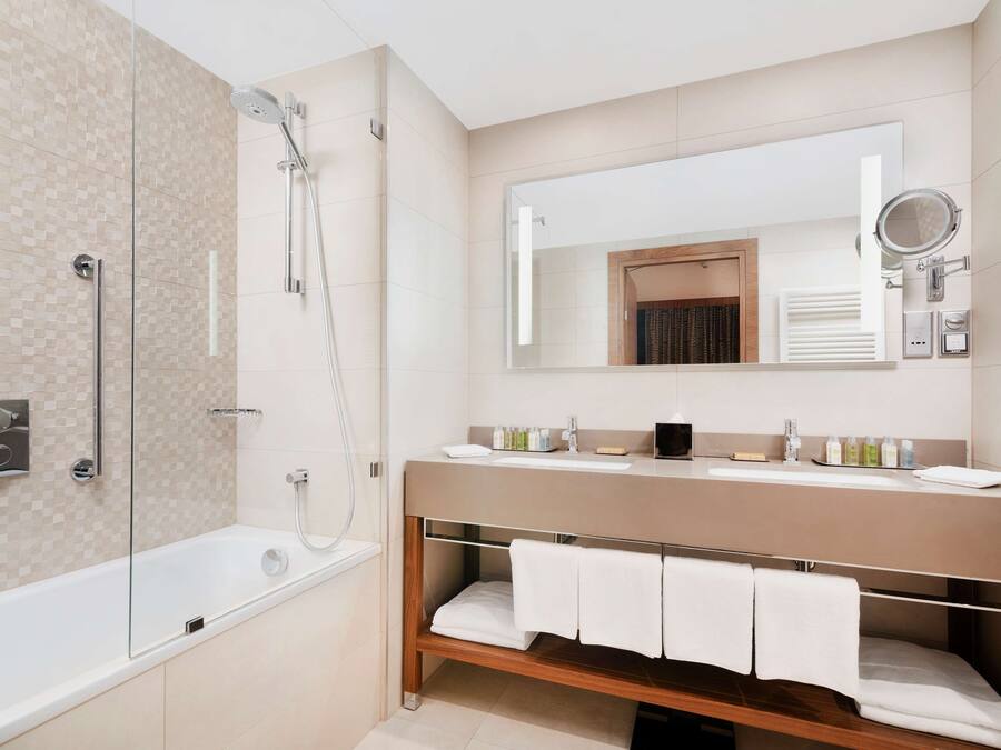 A modern bathroom with a glass-enclosed shower, a wooden vanity with a mirror, and a built-in shelf for towels.