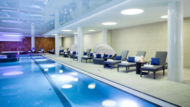 A modern indoor swimming pool with lounge chairs and a wooden wall. - DoubleTree by Hilton Krakow Hotel & Convention Center (Kraków)