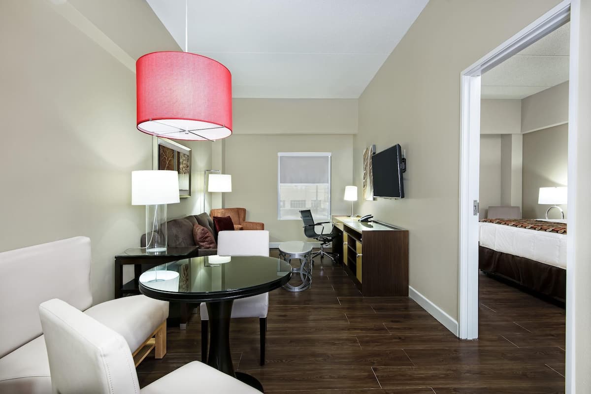 A hotel room with a dining area, a bed, a desk, and a TV.
