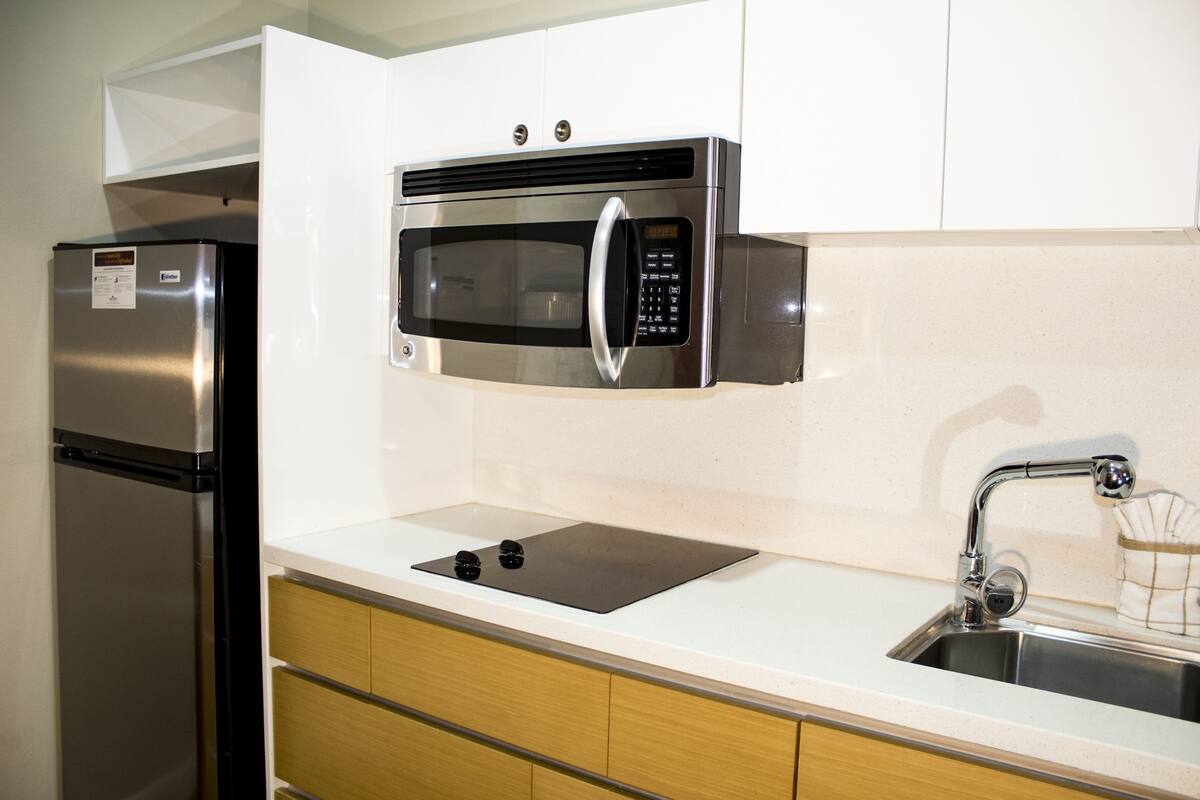 A kitchen with a stainless steel refrigerator, a microwave, a sink, and wooden cabinets.