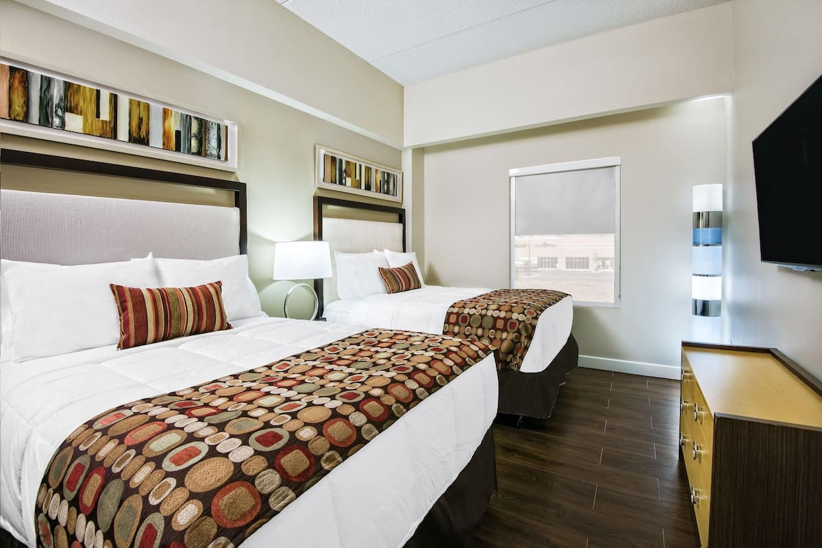 A hotel room with two beds, a TV, a window, and a bookshelf.