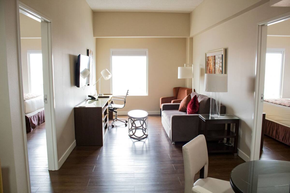 A modern living room with a sofa, a desk, a chair, a round table, and a TV mounted on the wall.