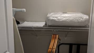 A compact utility room with a metal shelf holding a white pillow, a drying rack, and wooden hangers.