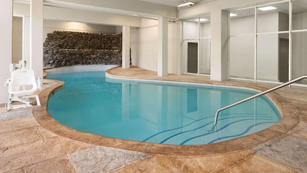 An indoor swimming pool with a stone wall backdrop, a poolside chair, and a clear blue pool. - Country Inn & Suites by Radisson, Gatlinburg, TN (Gatlinburg)