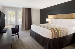 Habitación de hotel con cama, escritorio con computadora portátil, silla, televisor y ventana con cortinas.
