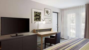 A hotel room with a bed, a desk, a TV, and a chair.