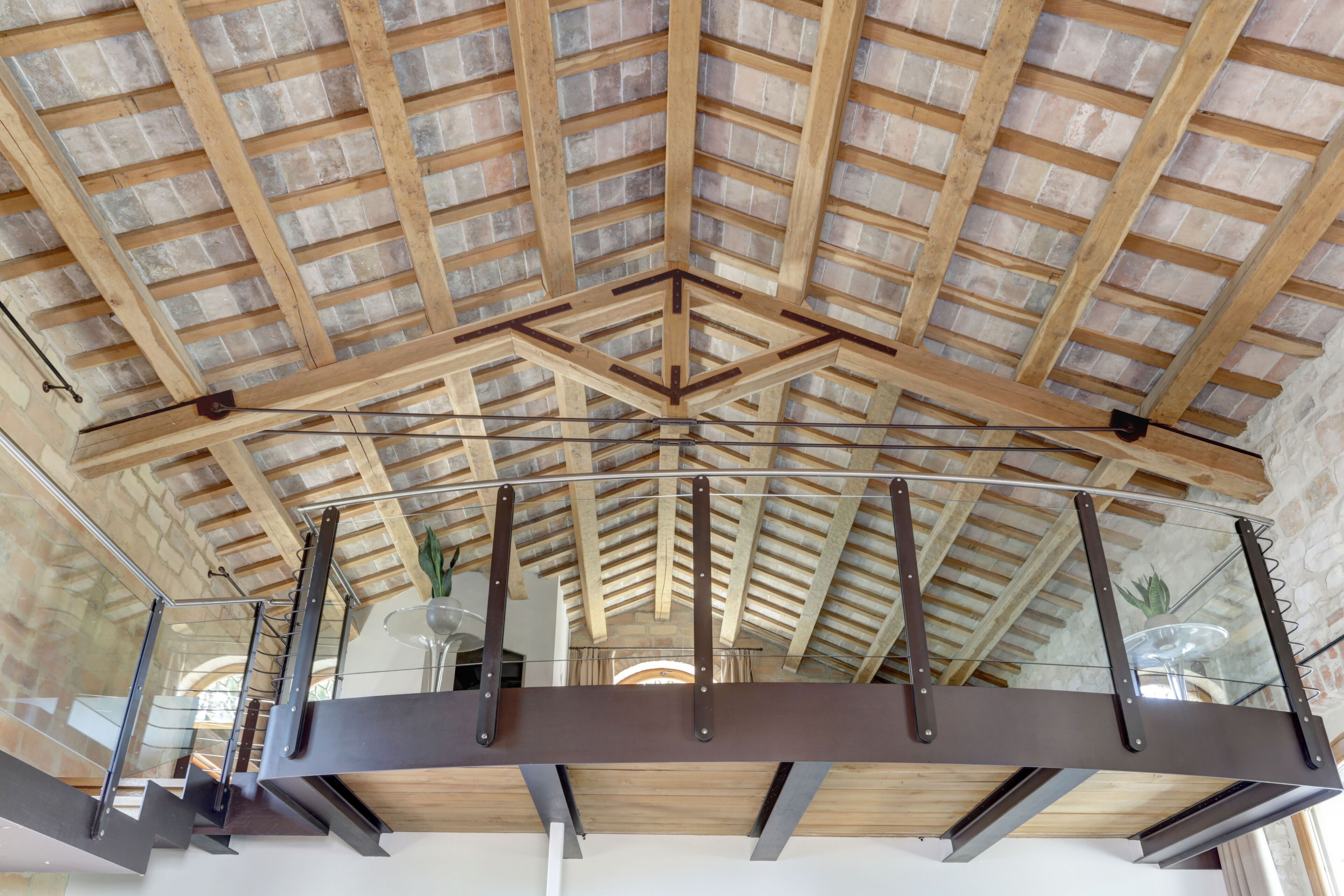 Un plafond haut avec des poutres en bois apparentes et une balustrade en verre.