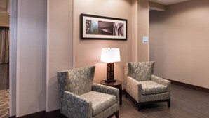 Une chambre d’hôtel avec deux fauteuils à motifs, une petite table avec une lampe et une œuvre d’art encadrée au mur.