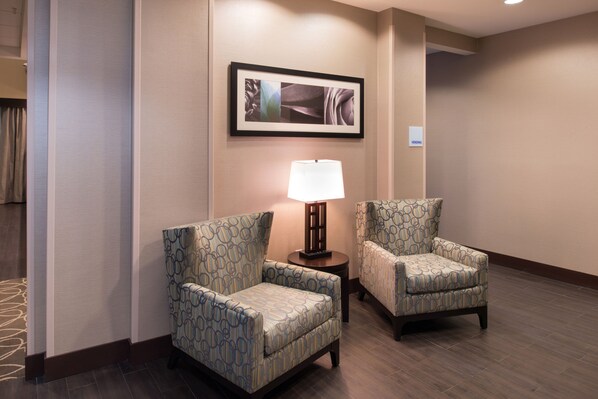 Une chambre d’hôtel avec deux fauteuils à motifs, une petite table avec une lampe et une œuvre d’art encadrée au mur.