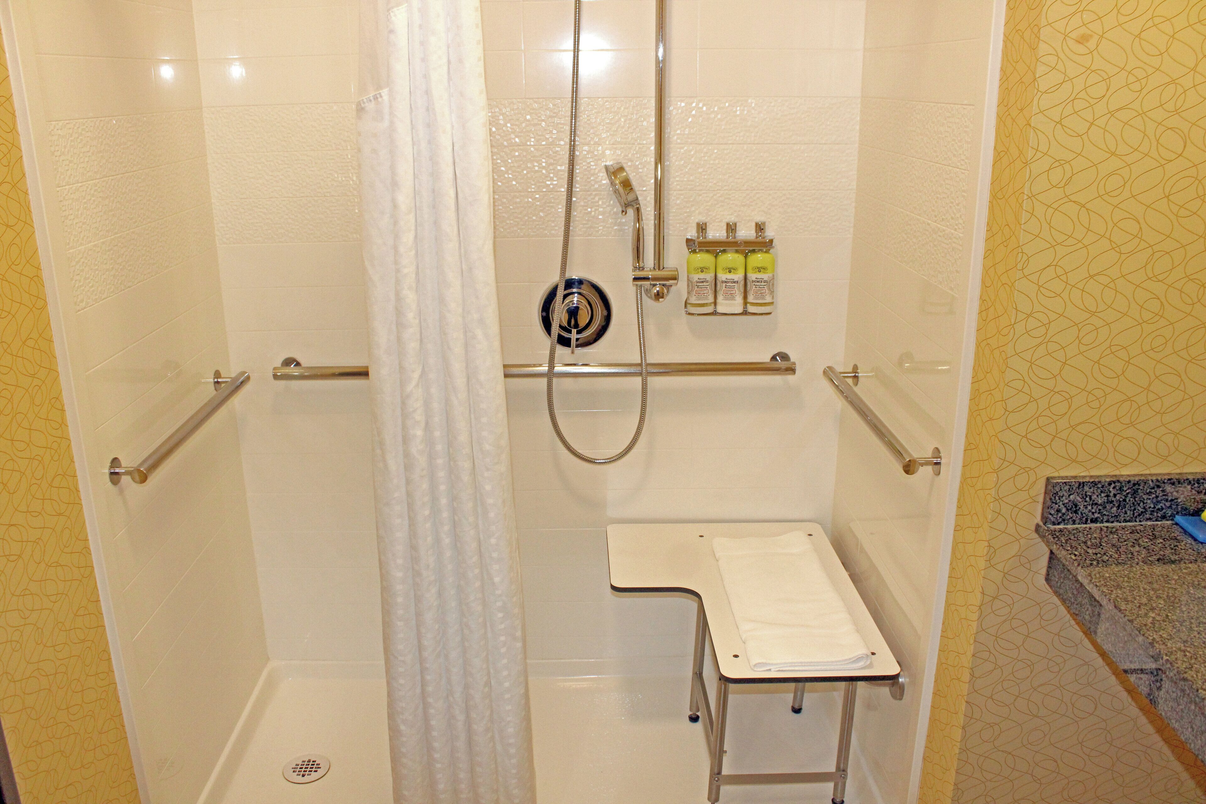 A shower with a handrail, a bench, and a wall-mounted bottle holder.