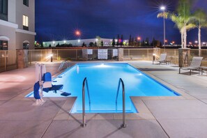 Una piscina exterior con un puesto de socorrista, una silla y un cartel que indica que no está permitido bucear.