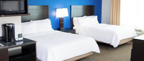 A hotel room with two beds, a microwave, a coffee maker, a lamp, and a nightstand.