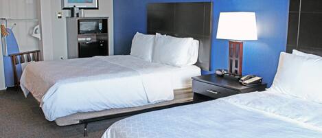 A hotel room with two beds, a desk with a lamp, a microwave, and a framed picture on the wall.