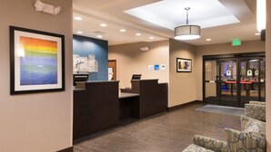 Een hotel receptie met een receptiebalie, een ingelijste kunstwerk aan de muur en gestoffeerde fauteuils in de zithoek.
