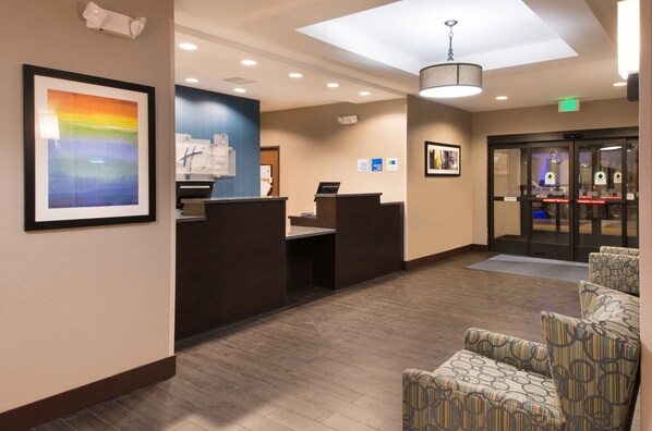 A hotel reception area with a reception desk, a framed artwork on the wall, and patterned chairs in the seating area. - Holiday Inn Express & Suites Bakersfield Airport by IHG (Bakersfield)