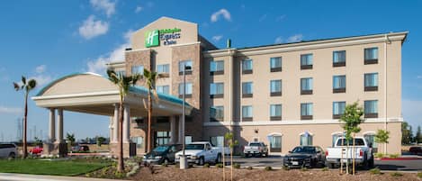 A Holiday Inn Express hotel with a covered entrance, multiple parking spaces, and a clear blue sky.