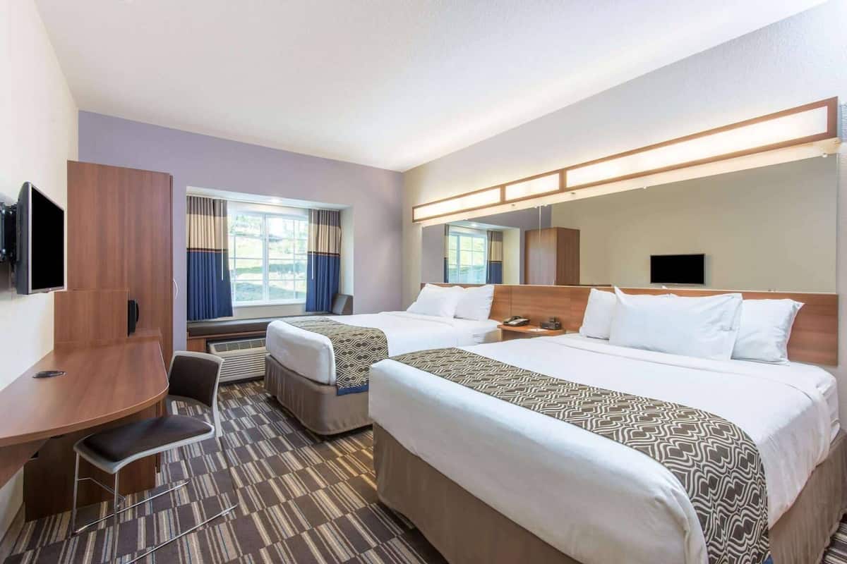A hotel room with two beds, a desk, a chair, a TV, and a window with curtains.