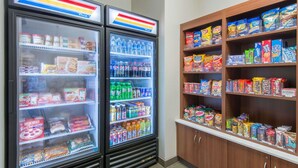 Two refrigerated display cases with various food and drink items, and adjacent shelves stocked with snacks and cereals. - Microtel Inn & Suites By Wyndham Cadiz (Cadiz)