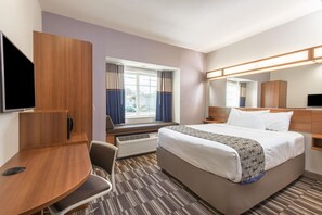 A hotel room with a bed, a desk, a chair, a television, a window with curtains, and a mirror. - Microtel Inn & Suites By Wyndham Cadiz (Cadiz)