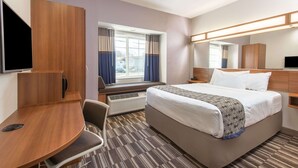 A hotel room with a bed, a desk, a chair, a TV, and a window with curtains. - Microtel Inn & Suites By Wyndham Cadiz (Cadiz)