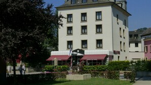 Un hotel de varios pisos con un llamativo toldo rojo, una estatua en la fachada y un jardín bien cuidado.