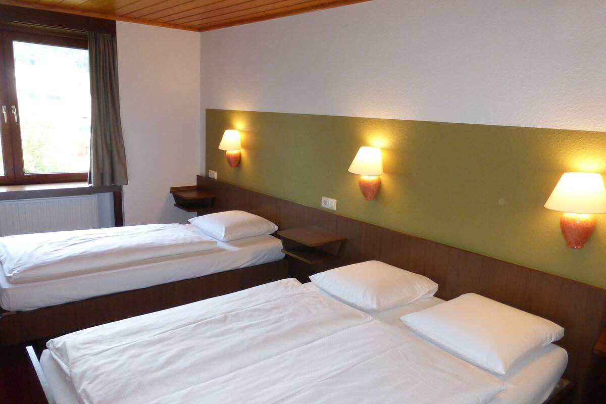 A hotel room with two single beds, a wooden headboard, and two wall-mounted lamps.