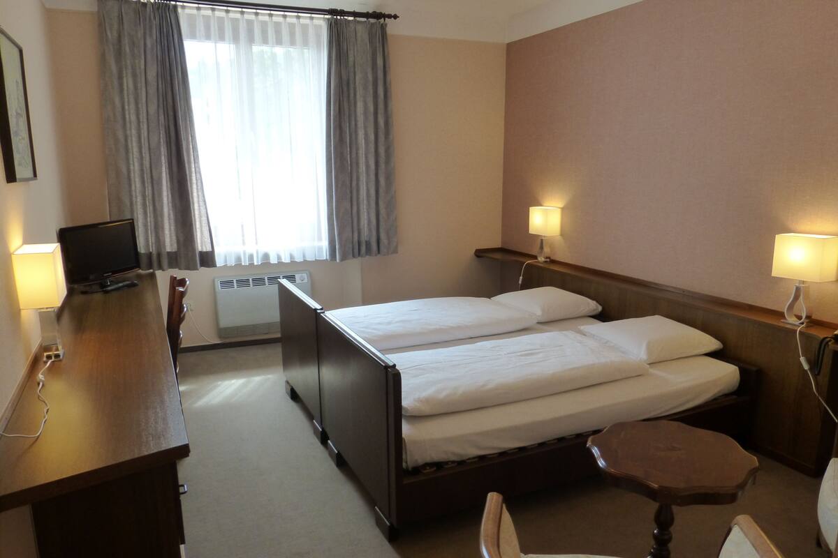 A hotel room with a bed, bedside lamps, a desk with a computer, and a chair.
