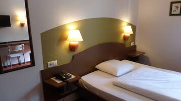A hotel room with a bed, two bedside lamps, a telephone, and a chair.