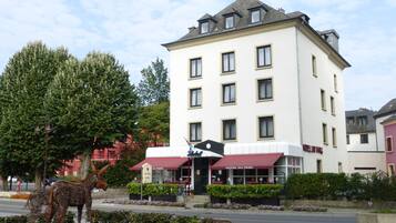 Un hotel con fachada blanca, múltiples ventanas y un toldo rojo.