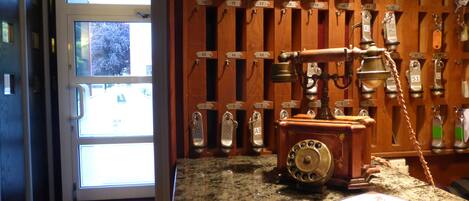 A room with a wooden wall displaying numbered keys, a vintage rotary phone, and a window with a view of the outside.