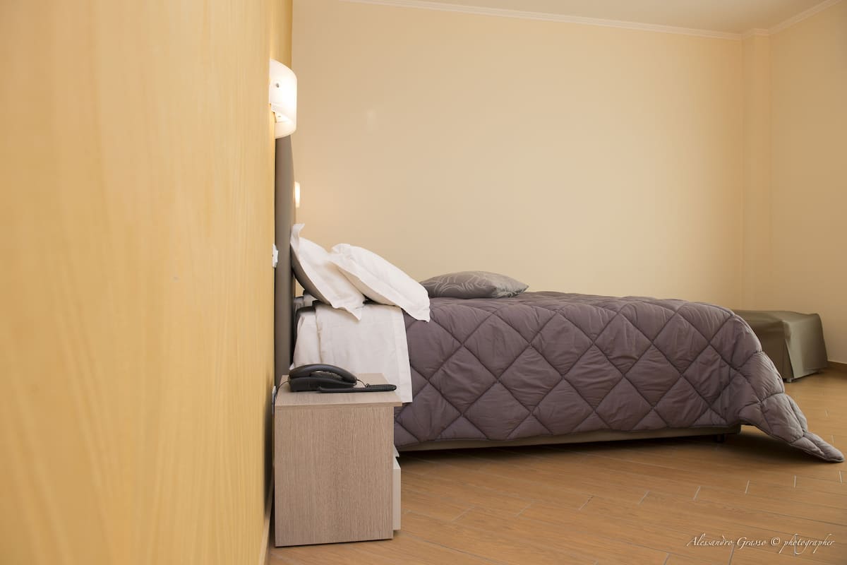 A hotel room with a bed, bedside table, and a lamp.