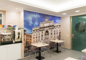 Camera d'albergo con un murale raffigurante un edificio storico, una macchina per caffè e due tavoli con sedie.