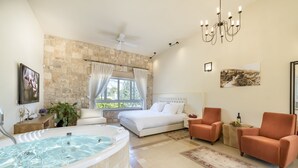 A spacious bedroom with a large bed, a sitting area with two armchairs, a bathtub, and a stone wall. - Villar (Rosh Pinna)