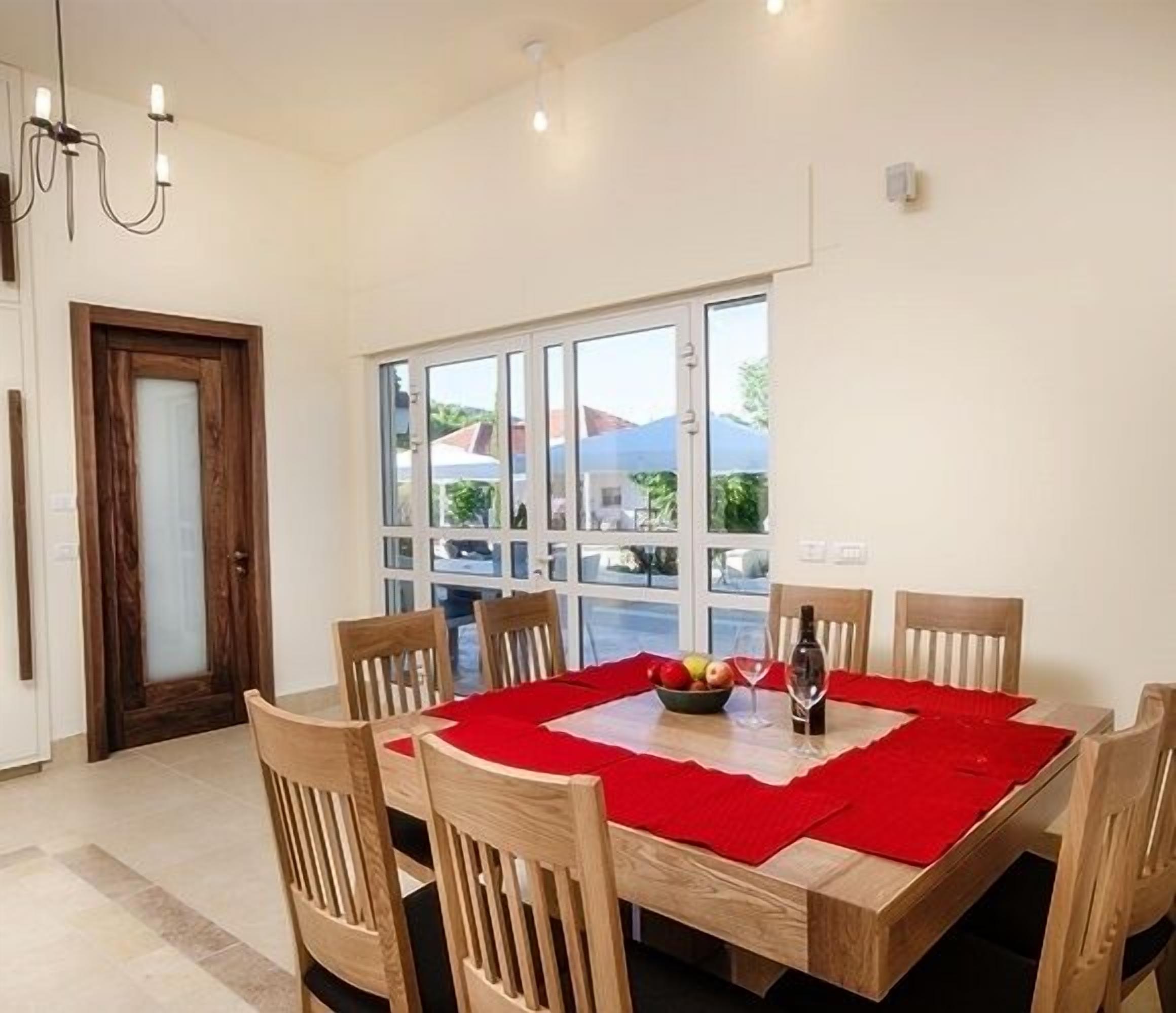 A dining area with a wooden table and chairs, a red table runner, and a bottle of wine.